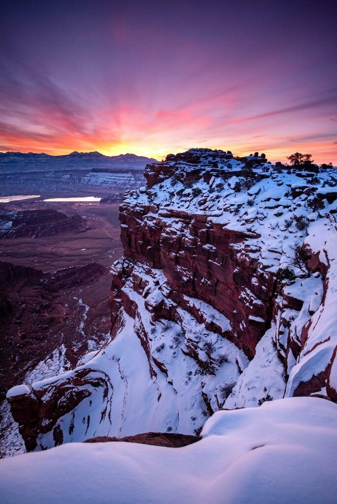 Color sunrise photo of a canyon in Utah with snow on the horizontal surfaces which contrasts with the dark-colored rock on vertical surfaces.