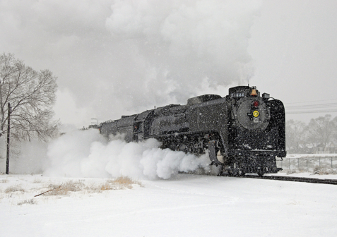 Black steam locomotive appears to be moving fast through a snowy scene.