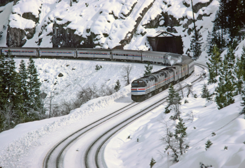 Color photo of an Amtrak passenger train in some snowy California mountains.